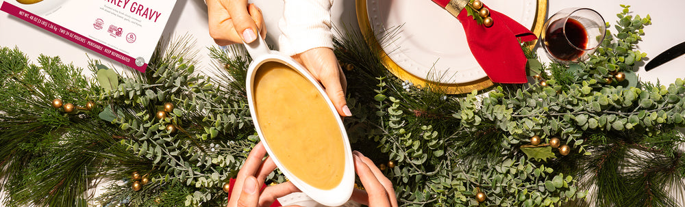 Someone passing a gravy boat of Kevin's Natural Foods Turkey Gravy over the top of an arrangement of Christmas decorations.