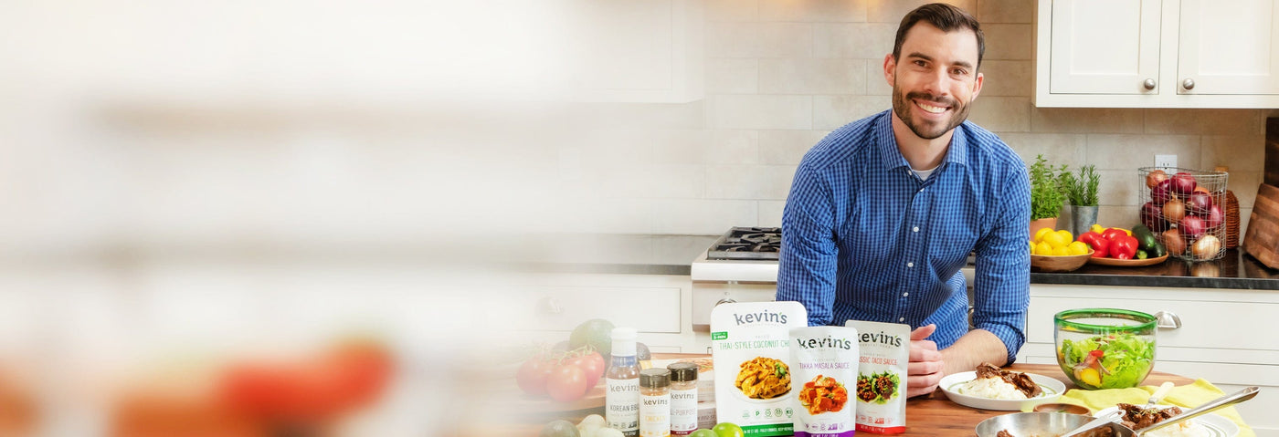 Kevin leaning against the kitchen counter with an arrangement of Kevin's products in front of him. 